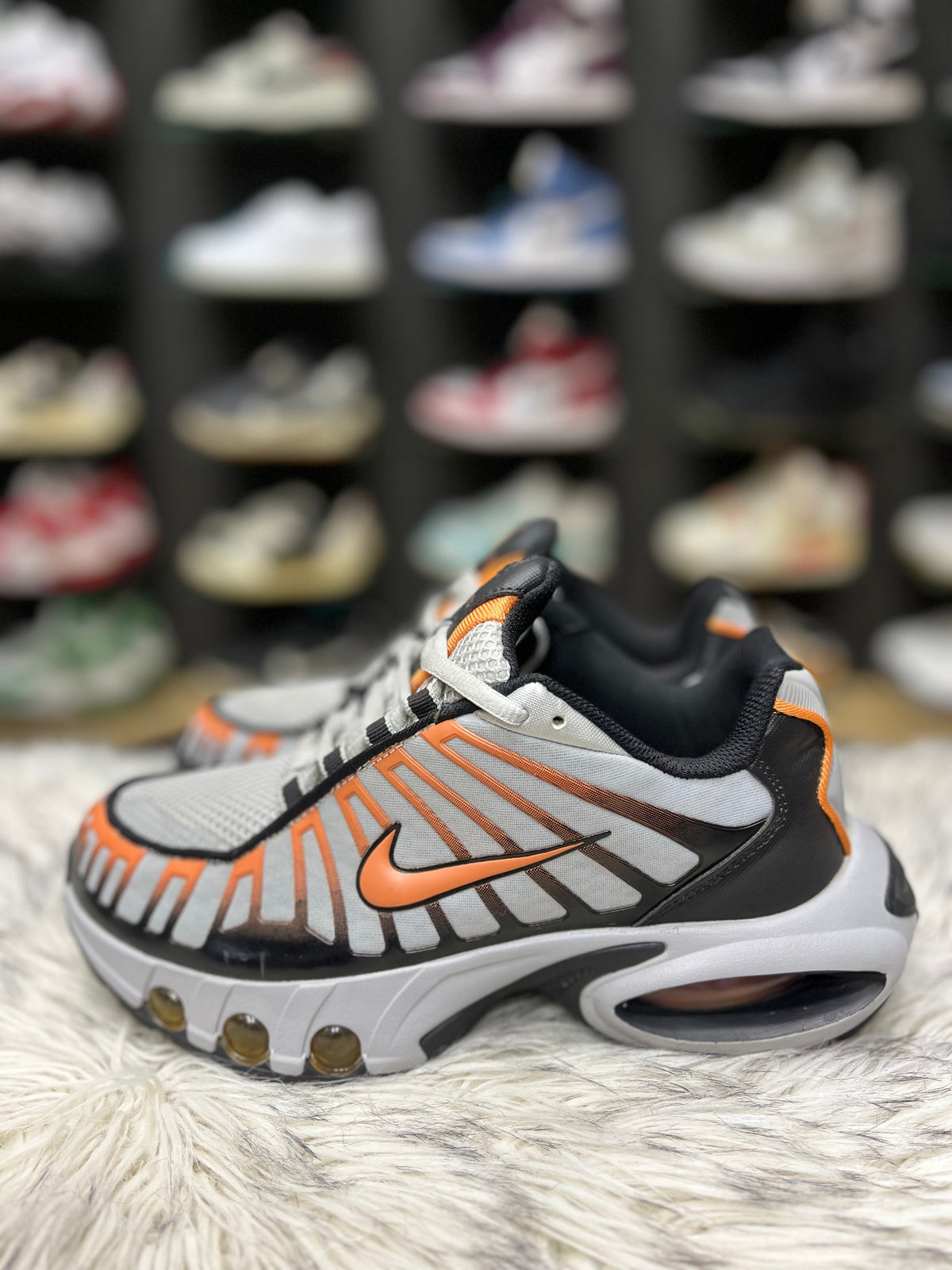 grey, black, and orange Nike Air Max Tailwind IV sneakers resting on a red Nike shoebox